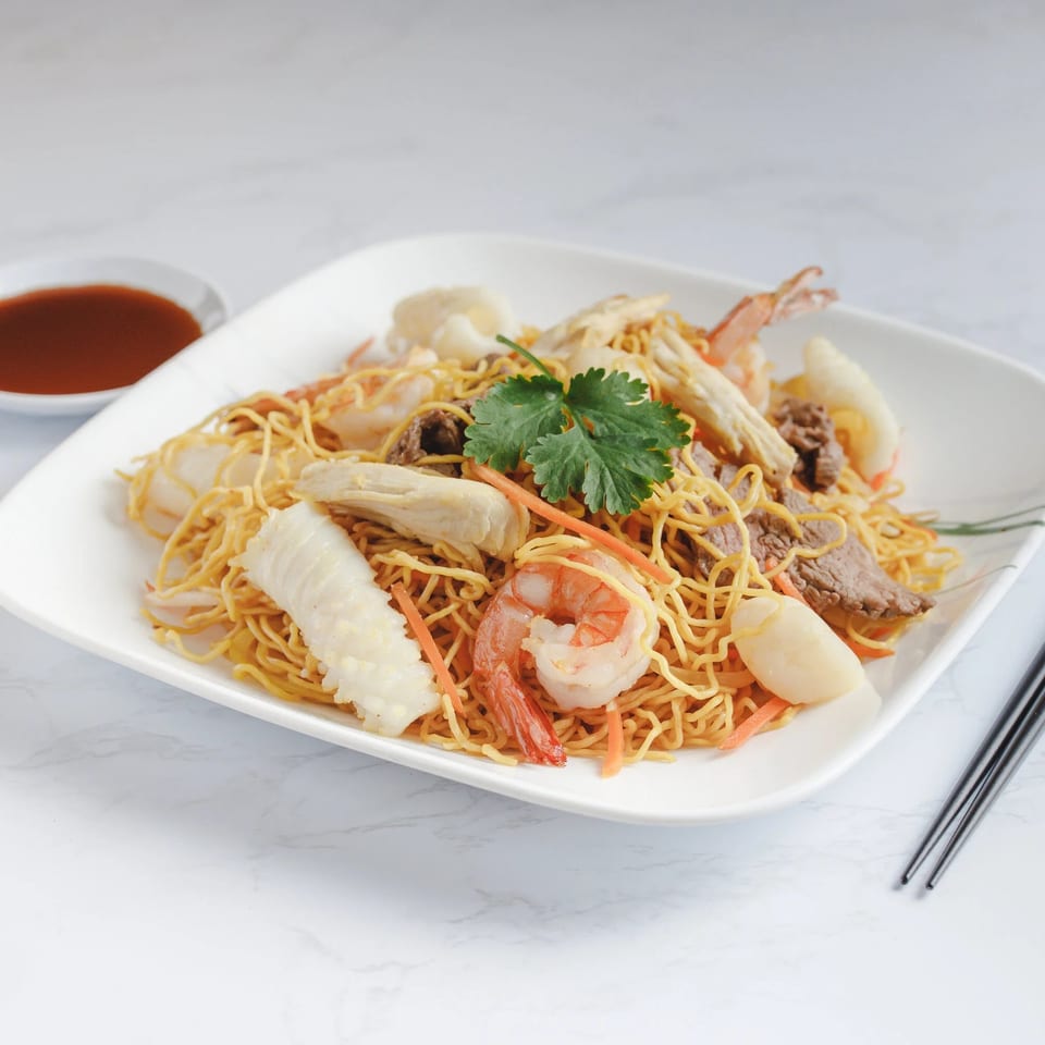 Vietnamese crispy egg noodles with shrimp, squid, beef, and vegetables, garnished with cilantro.