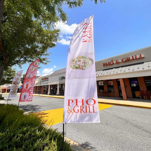 Pho & Grill restaurant exterior with promotional flags for pho and bubble tea under a blue sky.