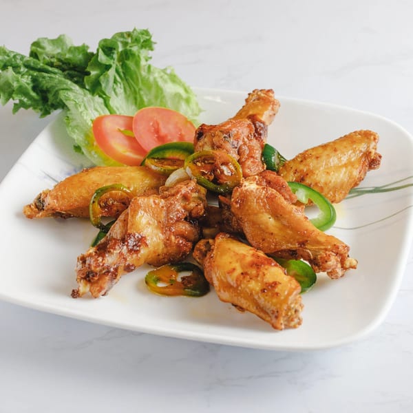 Vietnamese chicken wings with sliced jalapeños, onions, lettuce, and tomatoes on a white plate.
