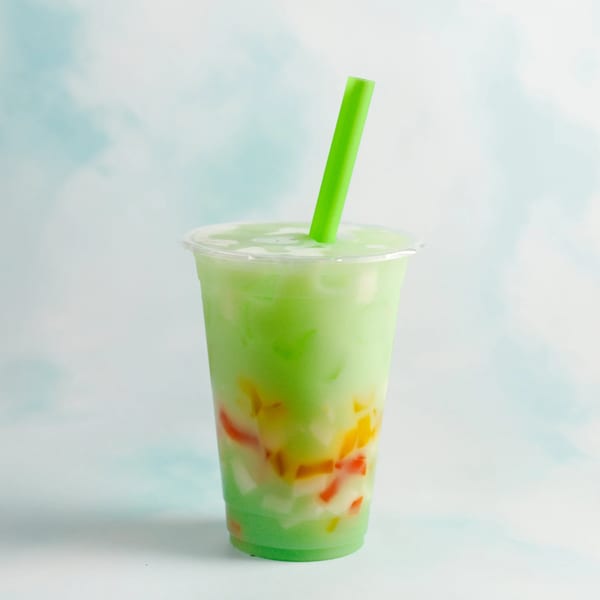 Green Vietnamese drink with colorful fruit jelly and a bright green straw in a clear cup.