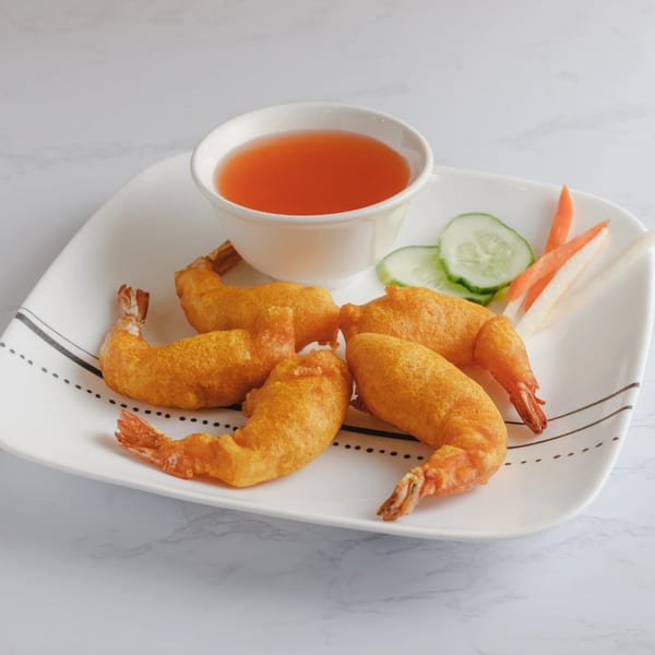 Five golden-brown fried shrimp with a side of dipping sauce, cucumber, and pickled carrots.