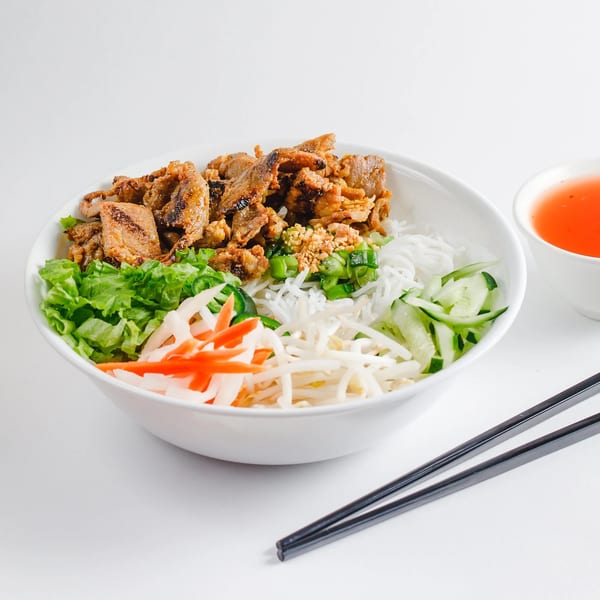 Vietnamese vermicelli bowl with grilled pork, fresh vegetables, and a side of sauce.