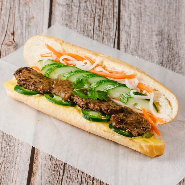 Vietnamese banh mi sandwich with grilled meat, cucumbers, pickled carrots, and jalapenos on parchment paper.