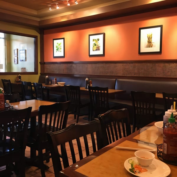Interior of Pho & Grill, showing dining tables, dark wooden chairs, and orange walls with framed art.