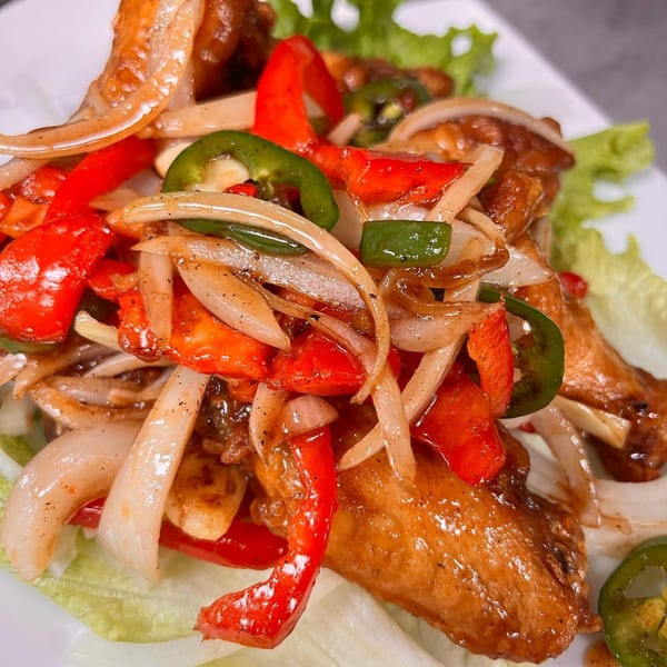 Vietnamese chicken wings with sautéed onions, red bell peppers, and green jalapeños on lettuce.