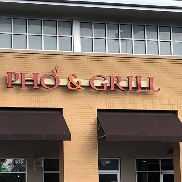 Pho & Grill restaurant sign on a brick building with brown awnings and windows above.