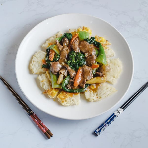 Vietnamese stir-fried beef and vegetables over crispy rice, served with decorative chopsticks.