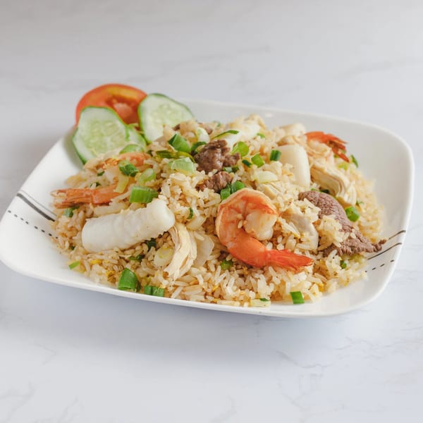 Vietnamese fried rice with shrimp, beef, chicken, squid, and vegetables, garnished with cucumber and tomato.